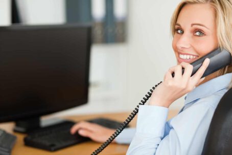 Young blonde businesswoman smiling into camera while on the phone in her office